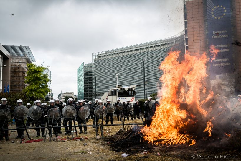 Police wearing riot gear and holding shields stand in front of a burning barricade as they protect the European Commission building in Brussels, Belgium during a protest by EU dairy farmers. September 7th, 2015. © Valentin Bianchi