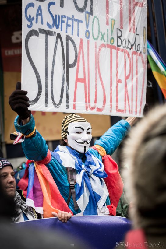 A demonstrator holds up a sign to protest against austerity measures outside of an EU summit in Brussels on Thursday, Oct. 15, 2015. Demonstrators blocked roads around the summit, where leaders were meeting nearby, to protest agains the Transatlantic Trade and Investment Partnership and European migration policies. (AP Photo/Valentin Bianchi)